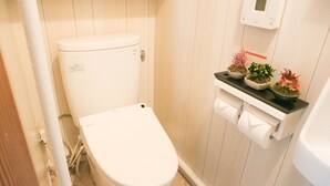 A small, clean bathroom with a toilet, a shelf with potted plants, and a toilet paper holder. - Wabi Sabi Kyoto (Kyoto)