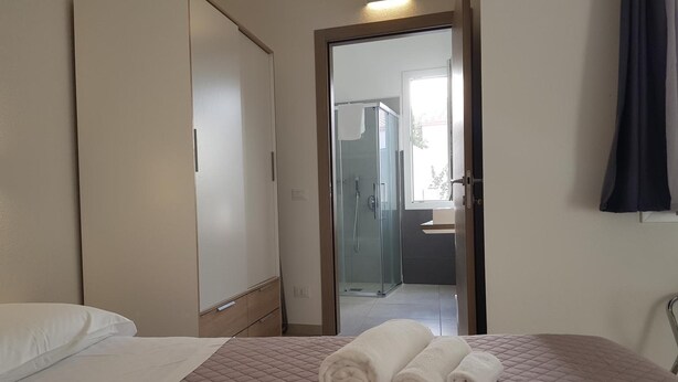 Una habitación de hotel con cama, armario y baño visible a través de una puerta abierta.