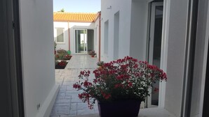 Un estrecho pasillo con suelo de baldosas que conduce a la entrada de un edificio. Hay macetas con flores rojas a lo largo del camino.