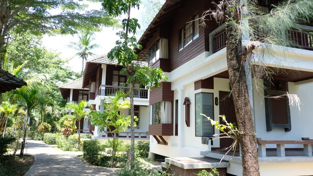A row of two-story villas with balconies, surrounded by lush greenery and palm trees.