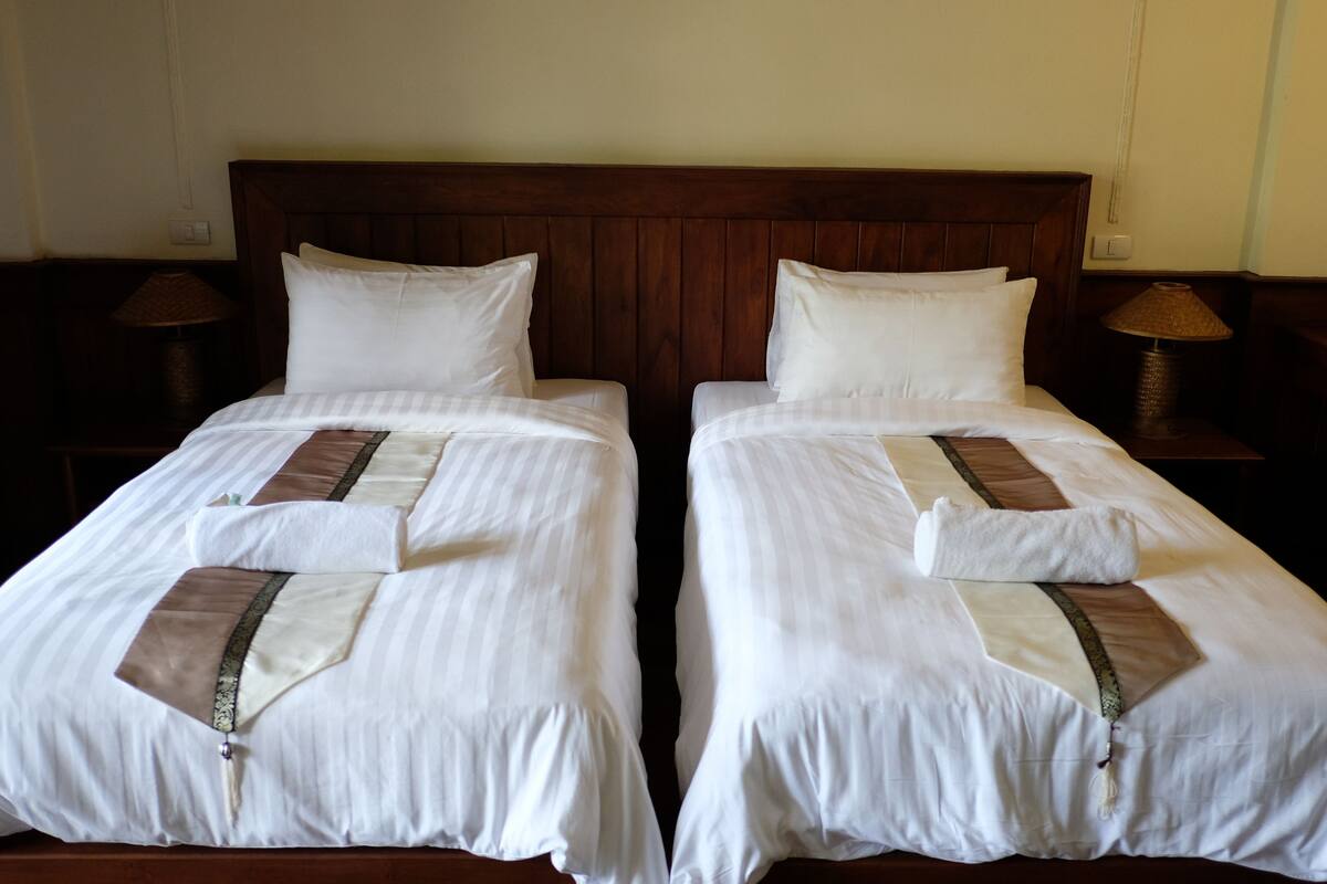 Un lit double avec du linge de lit blanc et une bande décorative marron, une tête de lit en bois et deux lampes de chevet.