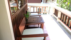A wooden bench with a white cushion on a balcony with a railing.