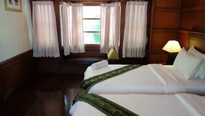 A hotel room with two beds, a wooden floor, a staircase, and a view of greenery outside.