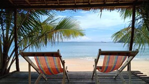 Two striped beach chairs facing a beach with palm trees and a clear view of the ocean.