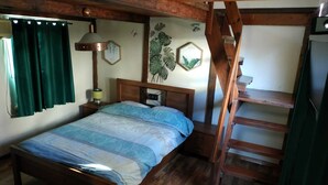 Un lit en bois, recouvert d’une couvre-lit à motifs bleus et blancs, dans une pièce aux murs et à l’échelle en bois.