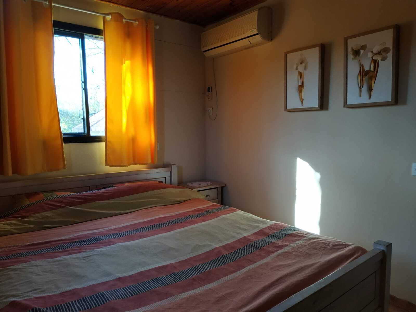 A bedroom with a bed, curtains, an air conditioning unit, and two wall-mounted pictures.