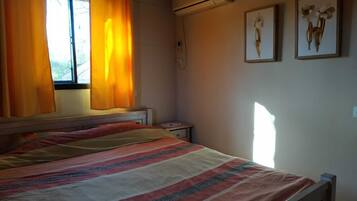 A bedroom with a bed, curtains, an air conditioning unit, and two wall-mounted pictures.