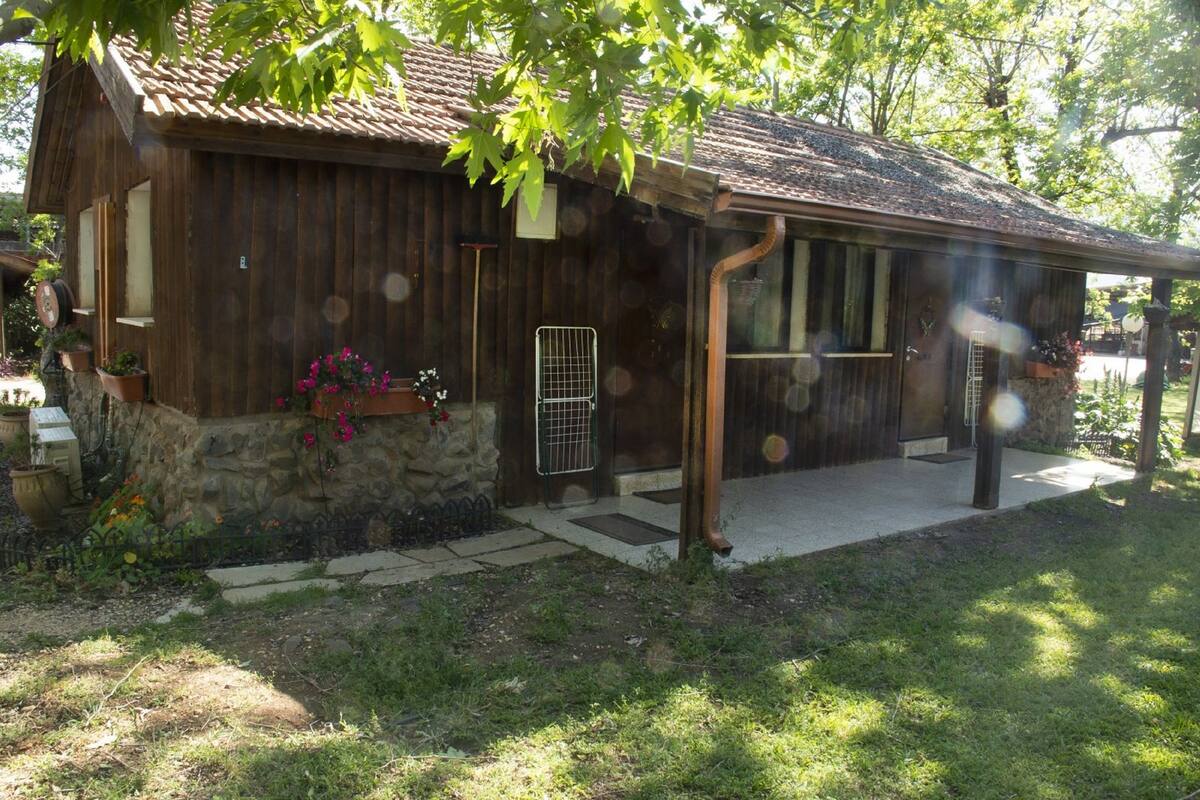A rustic wooden building with a stone foundation, a porch, and a small garden with potted plants and flowers.