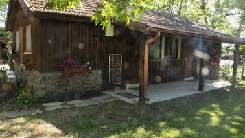 Un bâtiment rustique en bois, doté de fondations en pierre, d’un porche et d’un petit jardin agrémenté de plantes et de fleurs en pot.