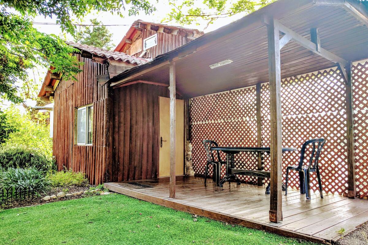 A wooden house with a covered porch, a small table, and two chairs.