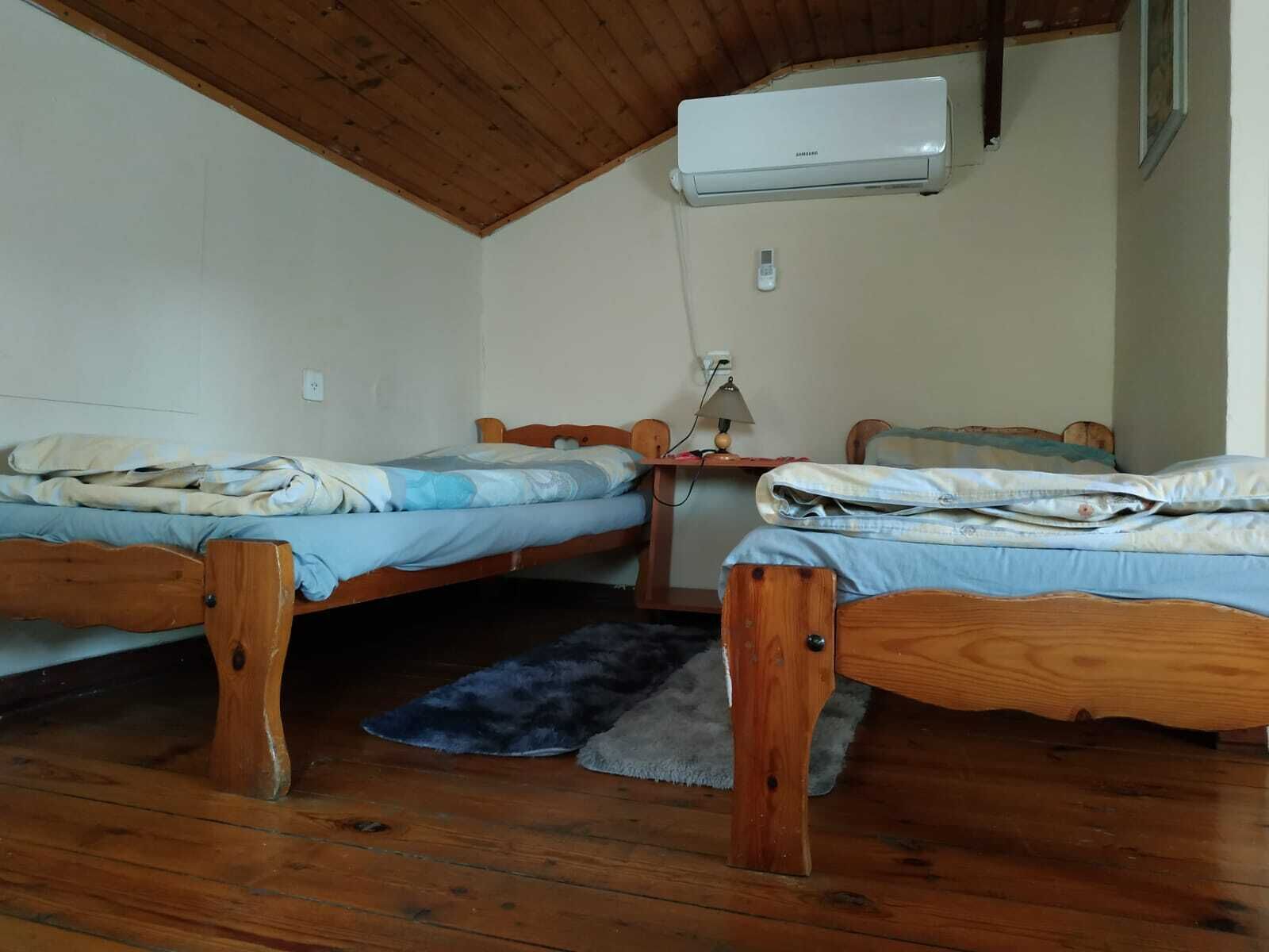 A small room with two wooden bunk beds, a desk with a lamp, and an air conditioning unit mounted on the wall.