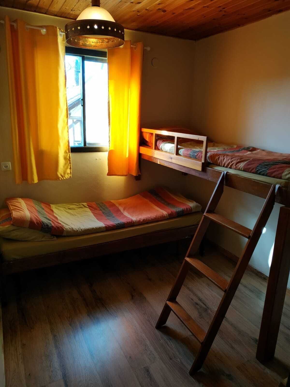 Una habitación pequeña con una cama nido, una escalera y un ventanal con cortinas.