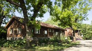 Un chalet rustique en bois, doté de fondations en pierre, entouré d’une végétation luxuriante et d’arbres.