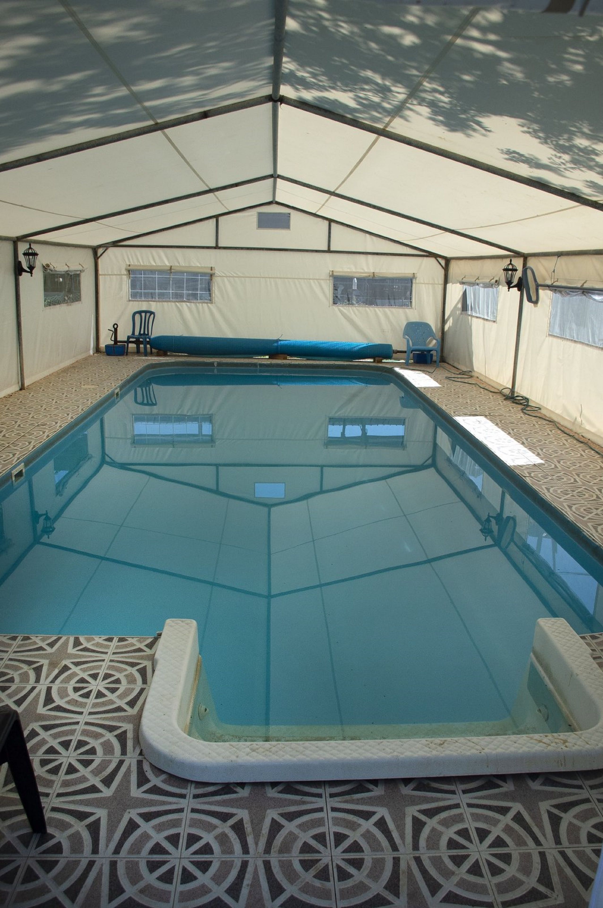 A covered swimming pool with a tiled floor, a bench, and a chair.