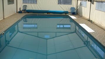 A covered swimming pool with a tiled floor, a bench, and a chair.