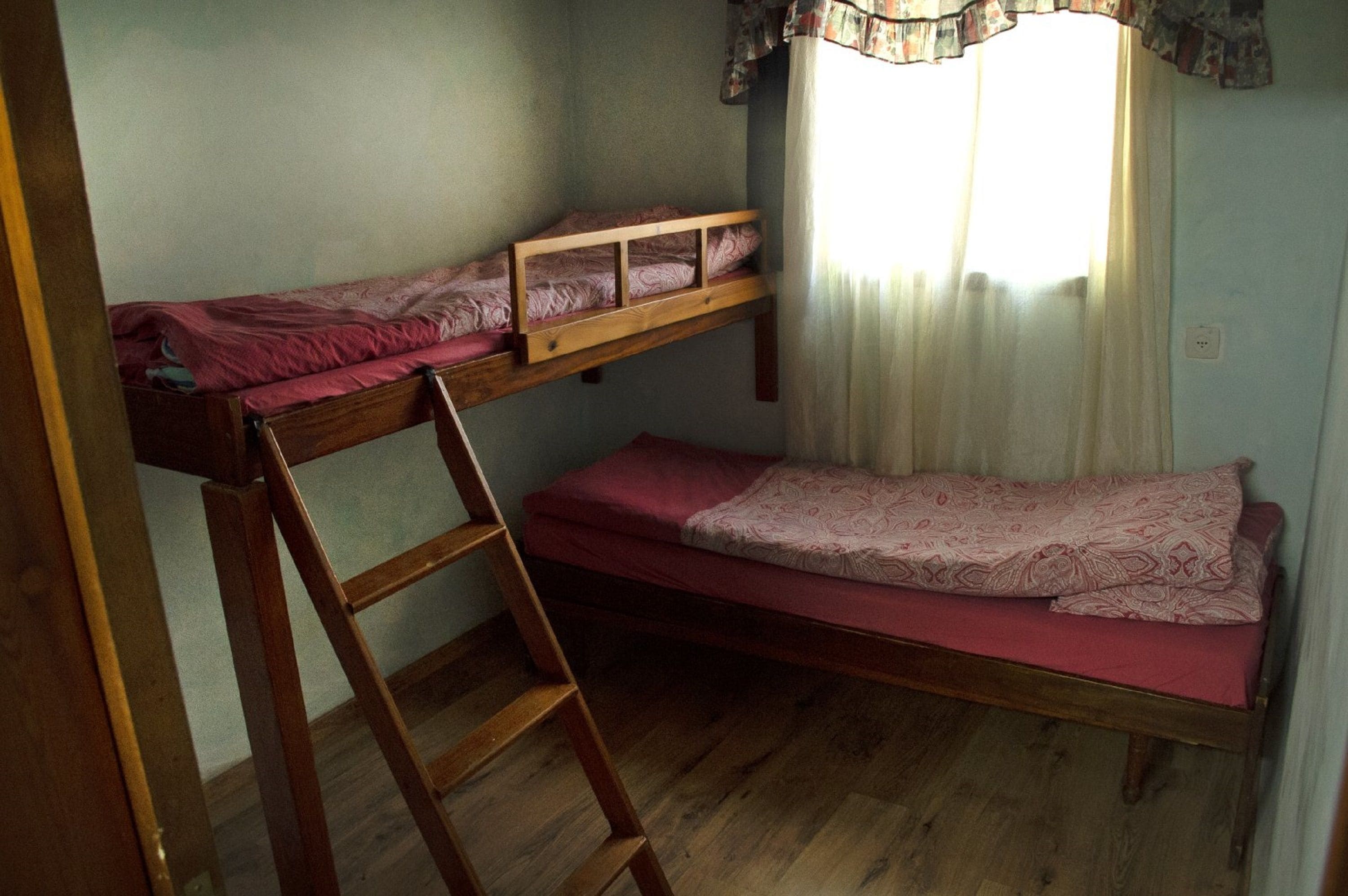 A small room with two bunk beds, a wooden ladder, and a window with curtains.