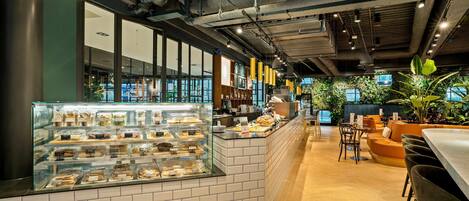 A modern cafe interior with a display case of pastries, a counter with a coffee machine, and seating area with a view of the outdoors.
