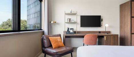 A hotel room with a bed, a desk, a chair, a TV, and a window with a view of a building.