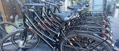 A row of bicycles parked in an outdoor area with a glass wall in the background.