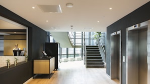 A modern reception area with a wooden counter, a staircase, and elevators. - Corendon Urban Amsterdam Schiphol Airport Hotel (Badhoevedorp)