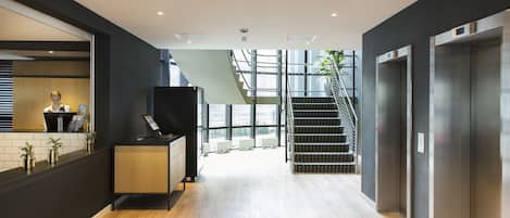 Una recepción moderna con mostrador de madera, una escalera y ascensores.
