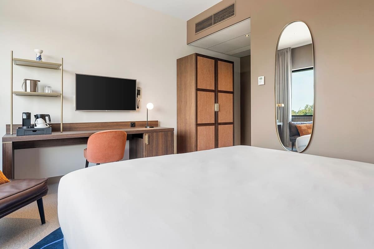 Ein Hotelzimmer mit Bett, Schreibtisch mit Stuhl, Fernseher, Kleiderschrank und Spiegel.