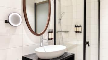 Uma casa de banho moderna com uma pia branca, um espelho grande e zona de duche com divisória de vidro.