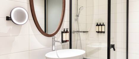 Un baño moderno con un lavamanos blanco, un espejo grande y una zona de ducha con mampara de cristal.