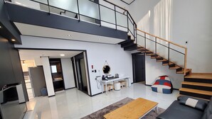 A modern living room with a sofa, a coffee table, a staircase, and a kitchen area. - The Stay Hostel (Yeosu)