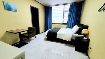 Una habitación de hotel con una cama, un escritorio, una silla y una ventana con cortinas.