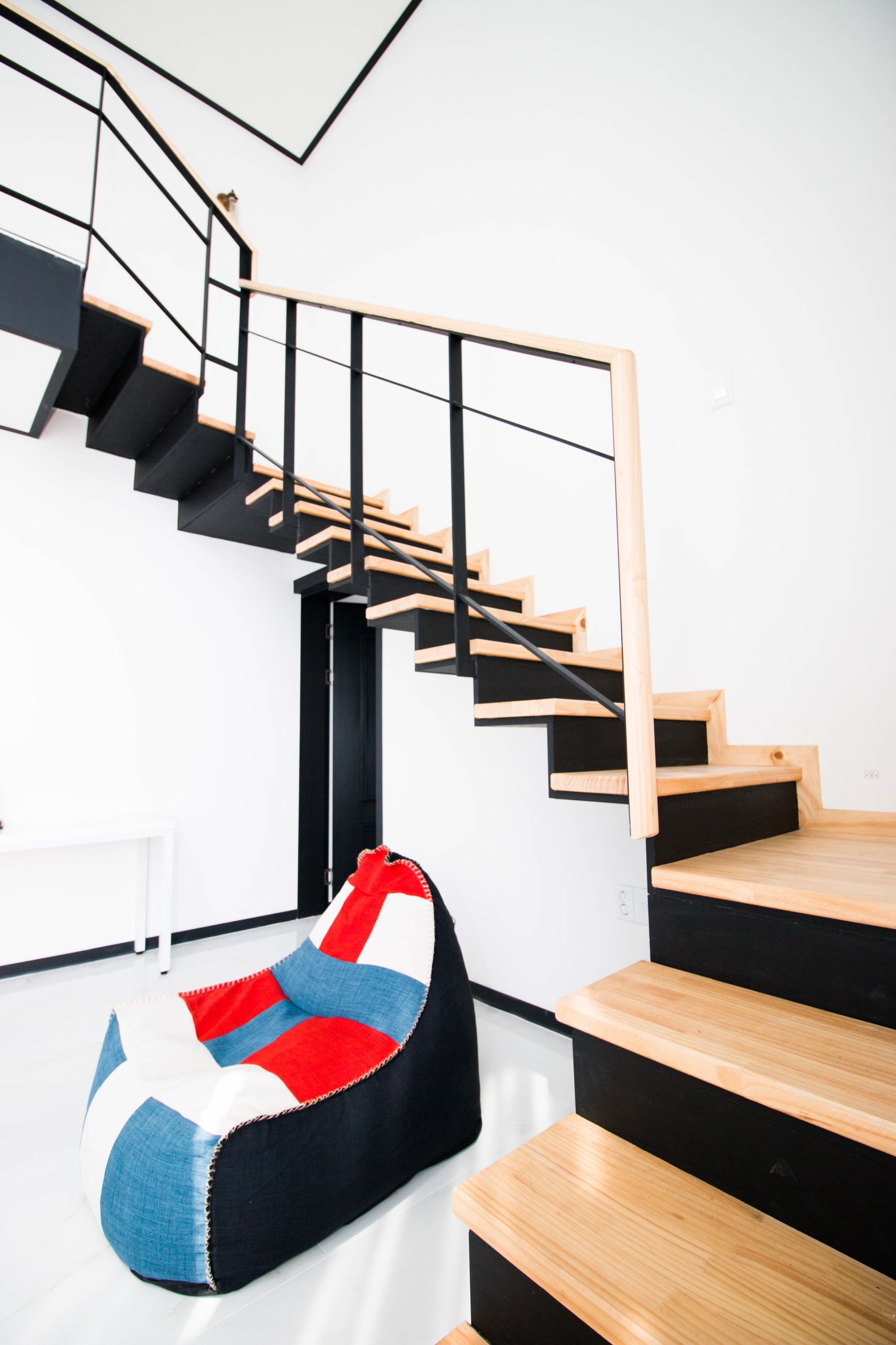 A modern interior with a staircase, a bean bag chair, and a white wall.