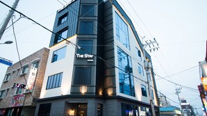A modern hotel with a prominent 'The Stay' sign, featuring a corner location with brick facade and large windows. - The Stay Hostel (Yeosu)