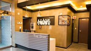 A reception desk with 'The Stay' signage, a patterned wall, and a door with a sign. - The Stay Hostel (Yeosu)
