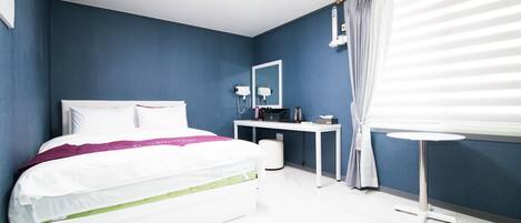 Una habitación de hotel moderna con cama, mesita de noche y un pequeño escritorio con silla.