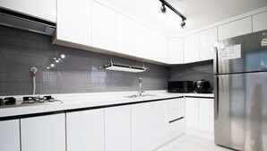 A modern kitchen with white cabinets, a stainless steel refrigerator, and a black coffee maker. - The Stay Hostel (Yeosu)
