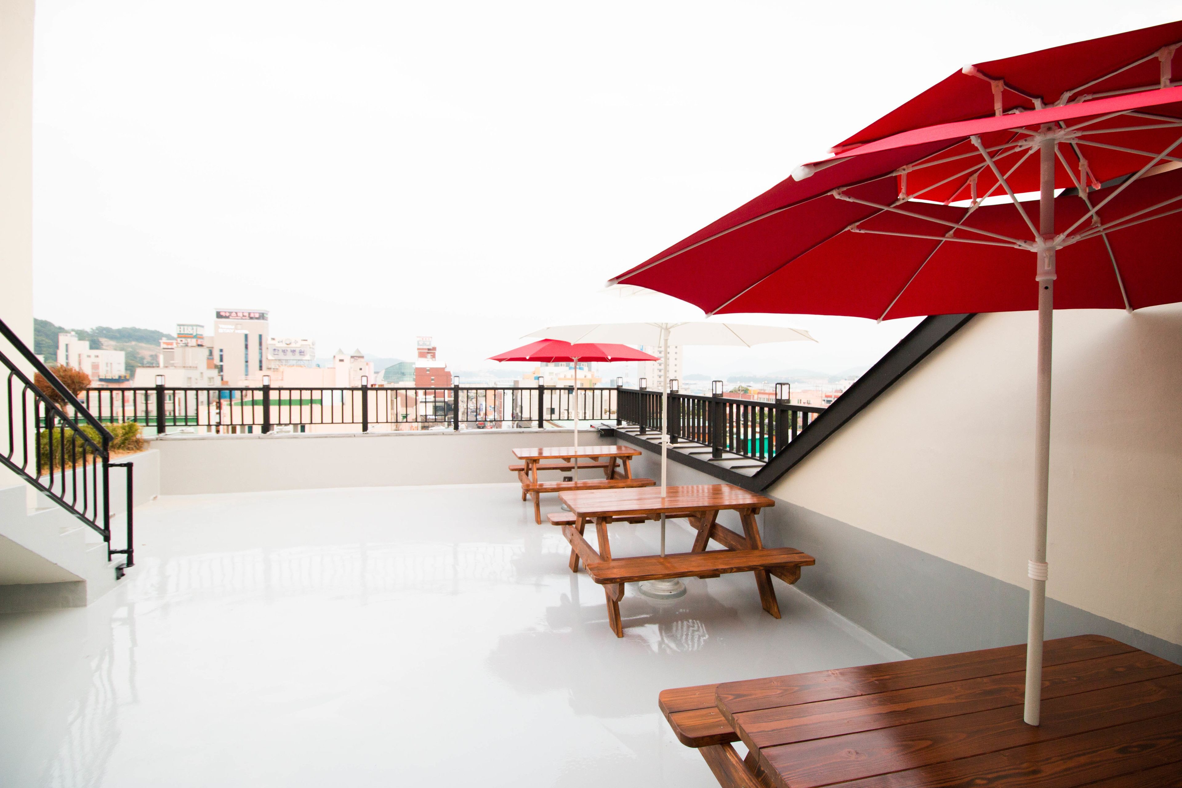 Terraza en la azotea con mesas de madera y sombrillas rojas, con vistas a la ciudad.