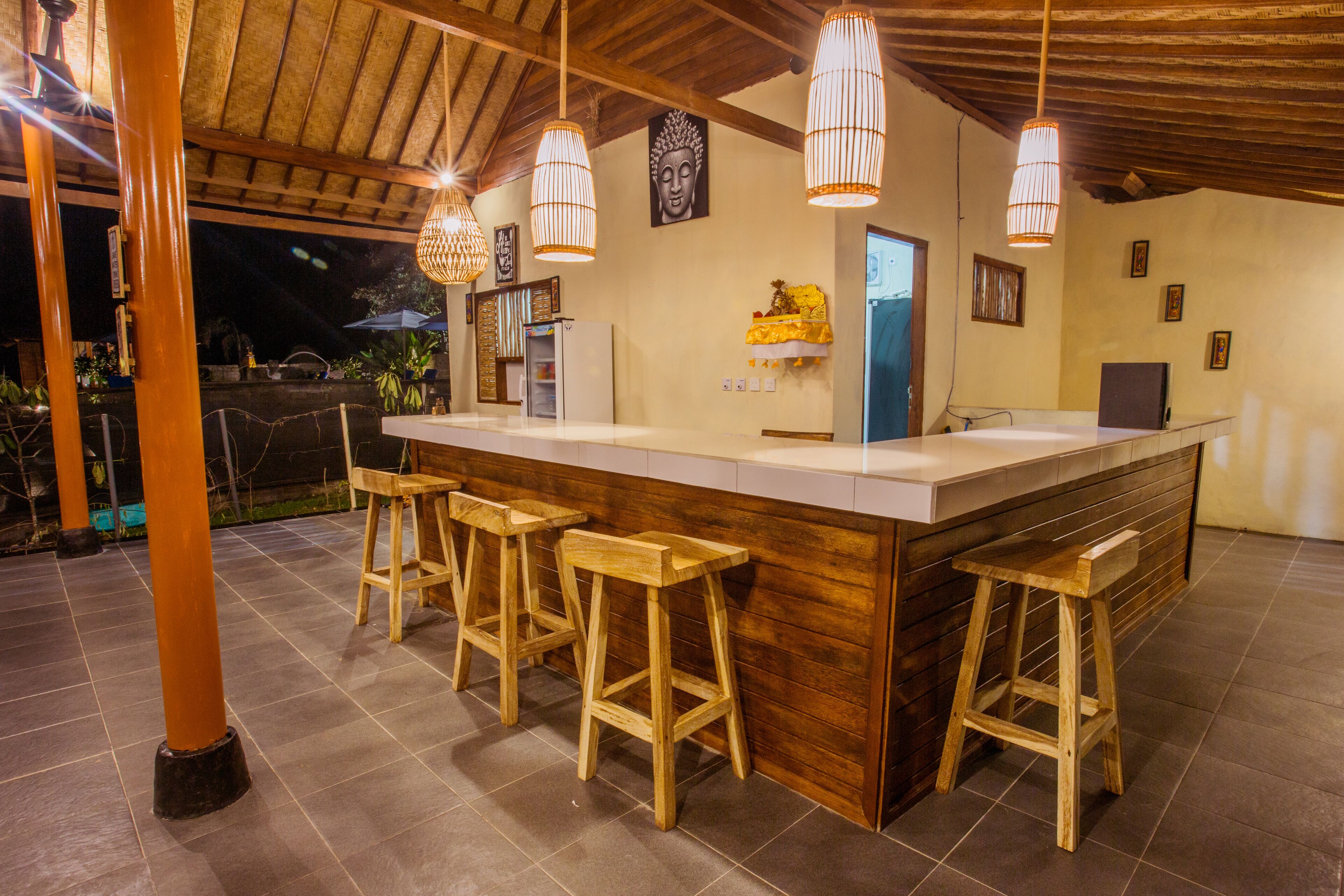 Una zona de bar con taburetes de madera, una barra, lámparas colgantes y una estatua de Buda en la pared.