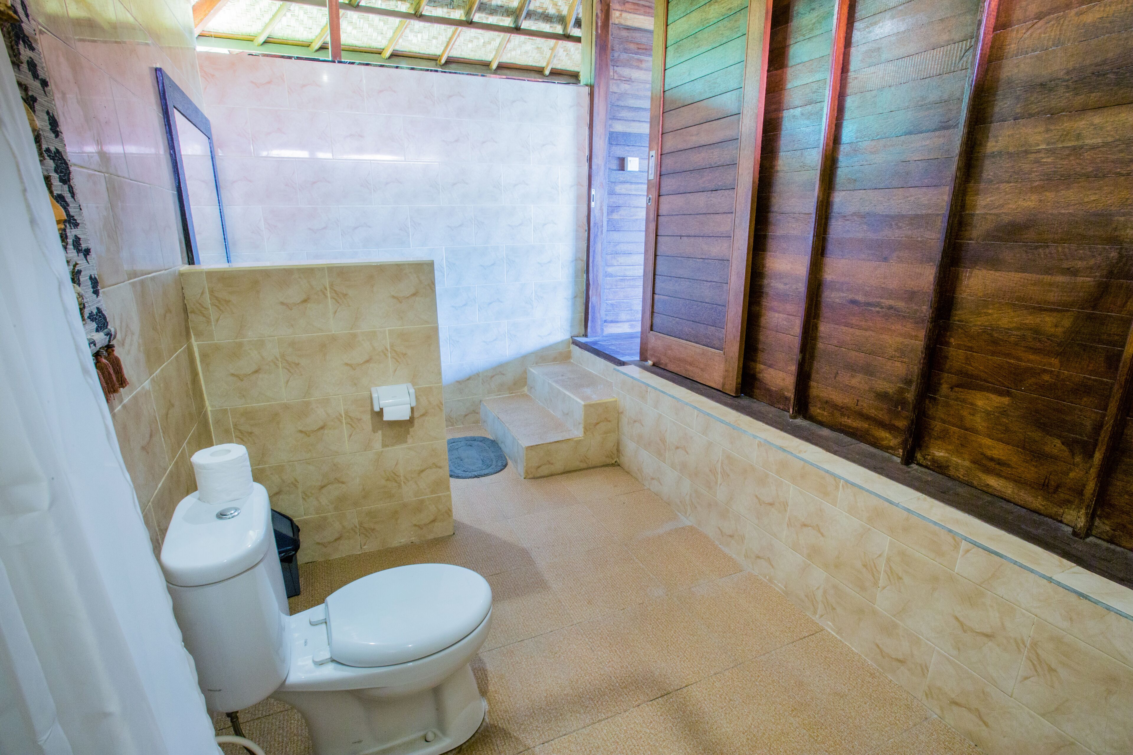 A small, tiled bathroom with a toilet, a shower area, and a wooden door.