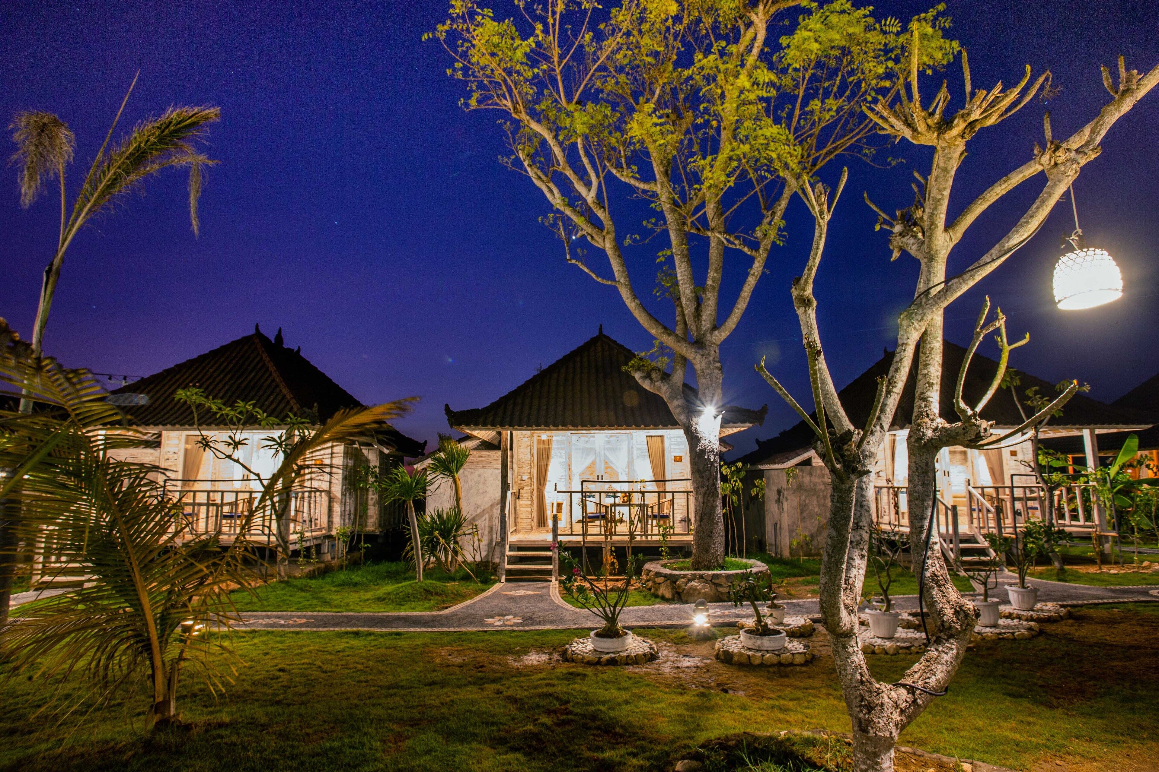 A well-lit resort with multiple buildings, a central pathway, and a variety of trees and plants.