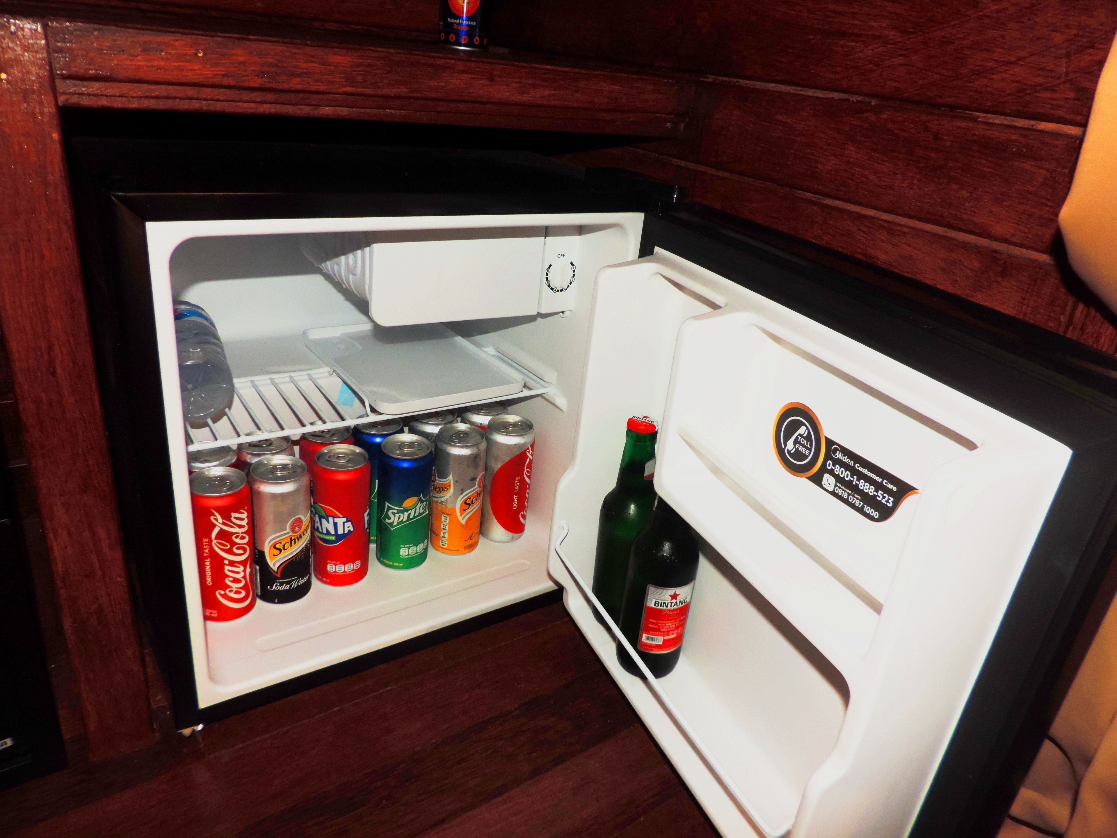 A small refrigerator with shelves containing various beverages and a bottle of Bintang beer.