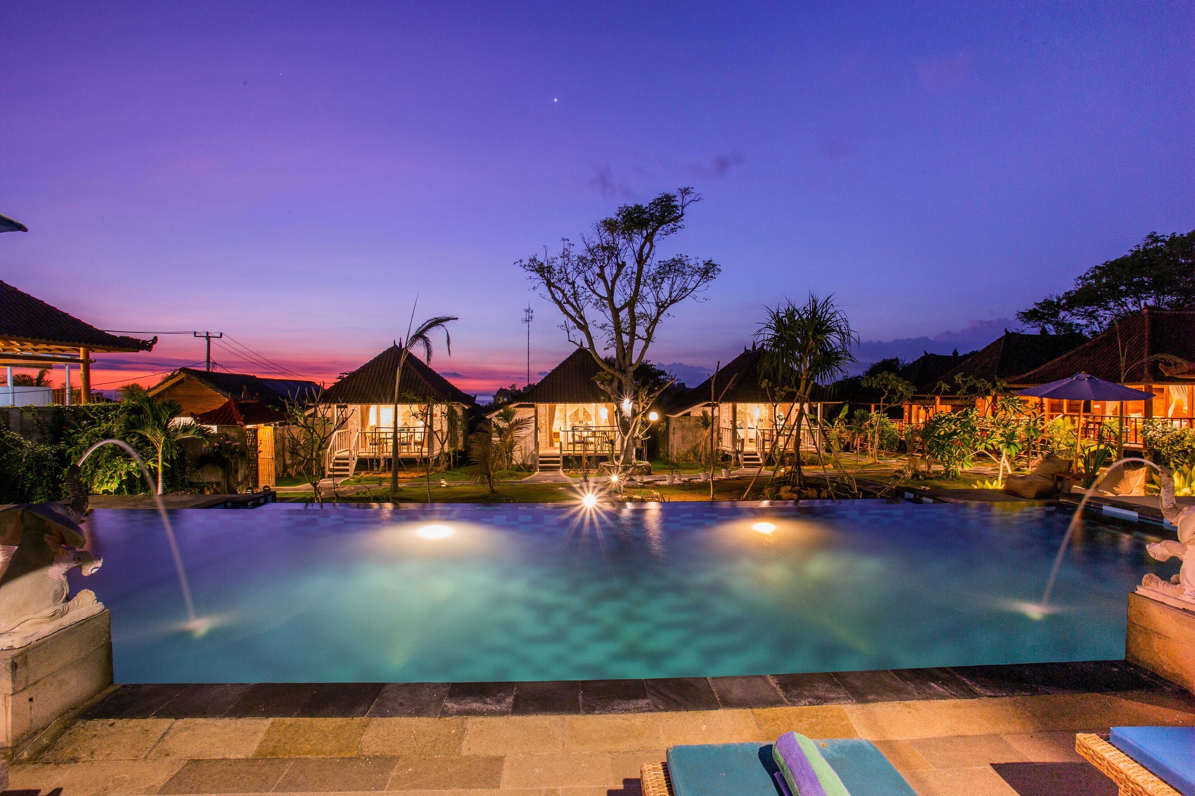 A swimming pool with a clear view of the surrounding area, including a building with a thatched roof and a tree in the center.