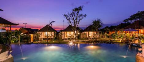 A swimming pool with a clear view of the surrounding area, including a building with a thatched roof and a tree in the center.