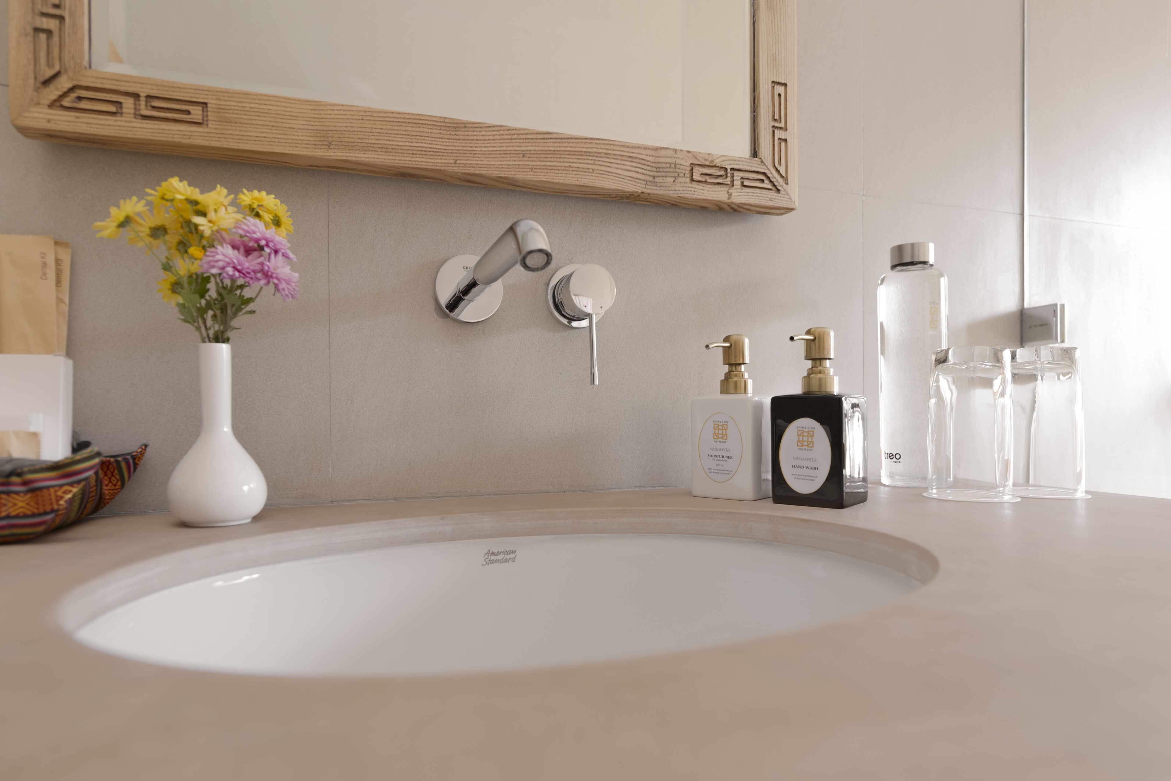 A bathroom with a white sink, a mirror with a wooden frame, a vase with flowers, and toiletries.