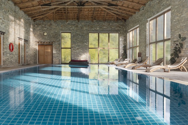 Una piscina techada, sombrillas, sillones reclinables de piscina