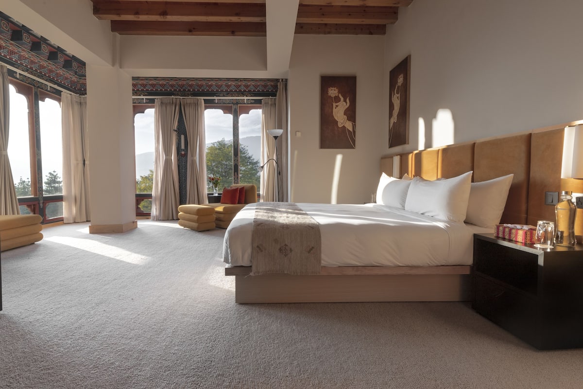 Quarto com cama grande, mesa de cabeceira, cadeira e vista para o exterior.