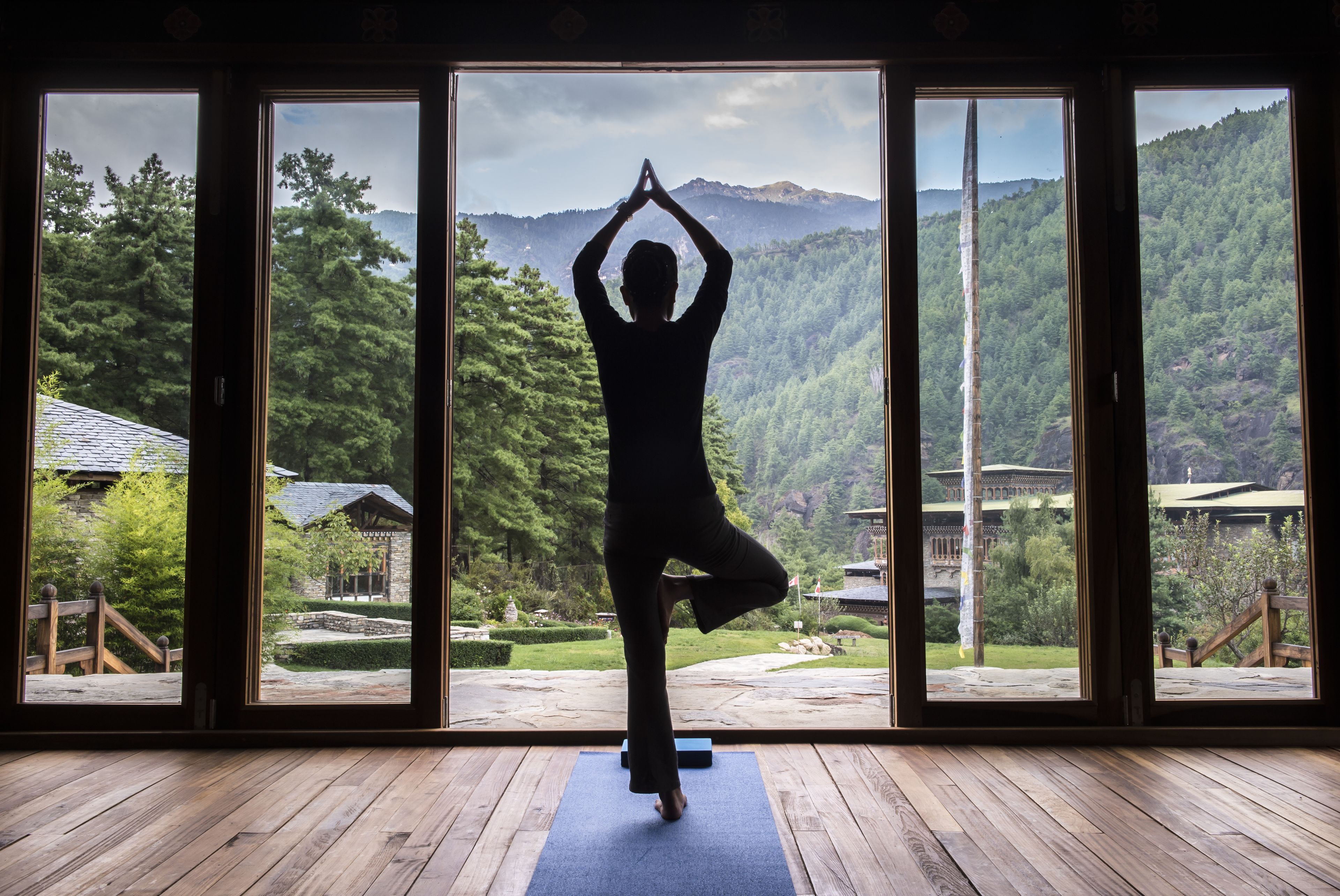 Une personne pratiquant le yoga dans une pièce dotée de grandes fenêtres donnant sur un paysage montagneux.