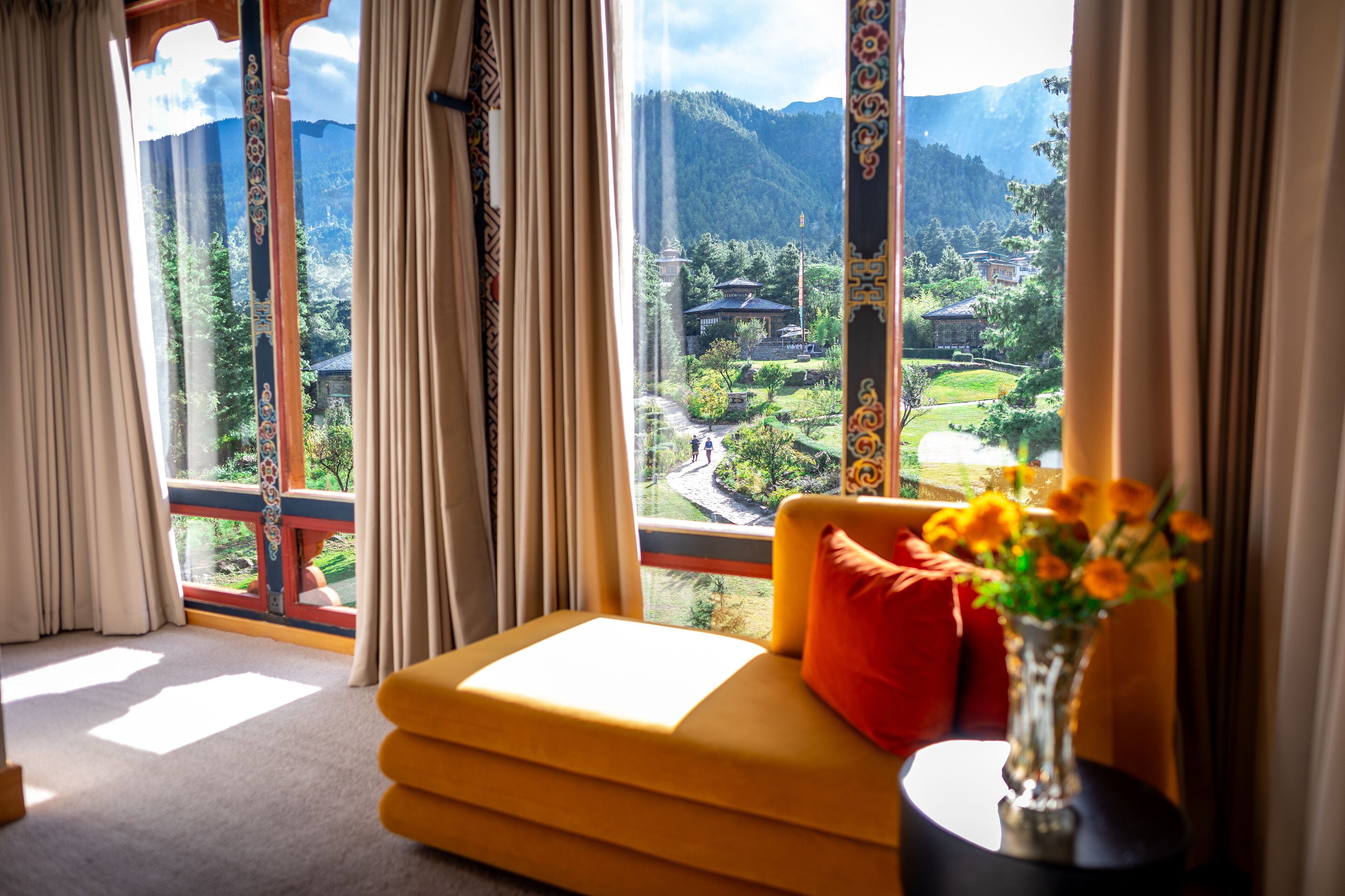 Una habitación con sofá, un jarrón con flores y vistas a un paisaje montañoso a través de amplias ventanas.