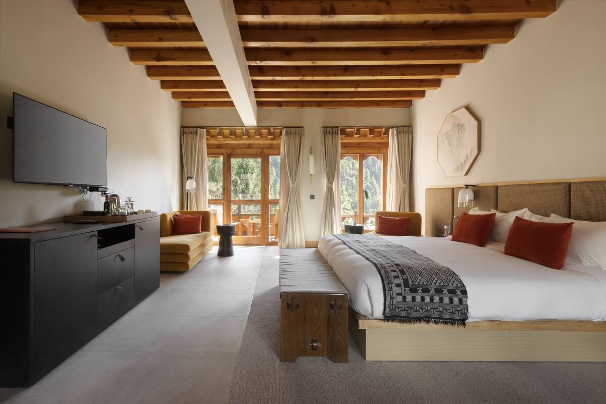 Quarto com uma cama grande, televisão, teto de madeira e vista para o exterior.