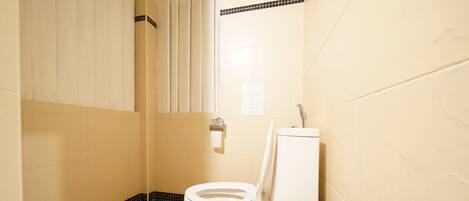 A small, clean bathroom with a toilet, a trash bin, and a shower area.