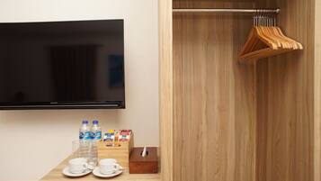 A hotel room with a flat-screen TV mounted on the wall, a wooden table with a tissue box, two cups, and two bottles of water.